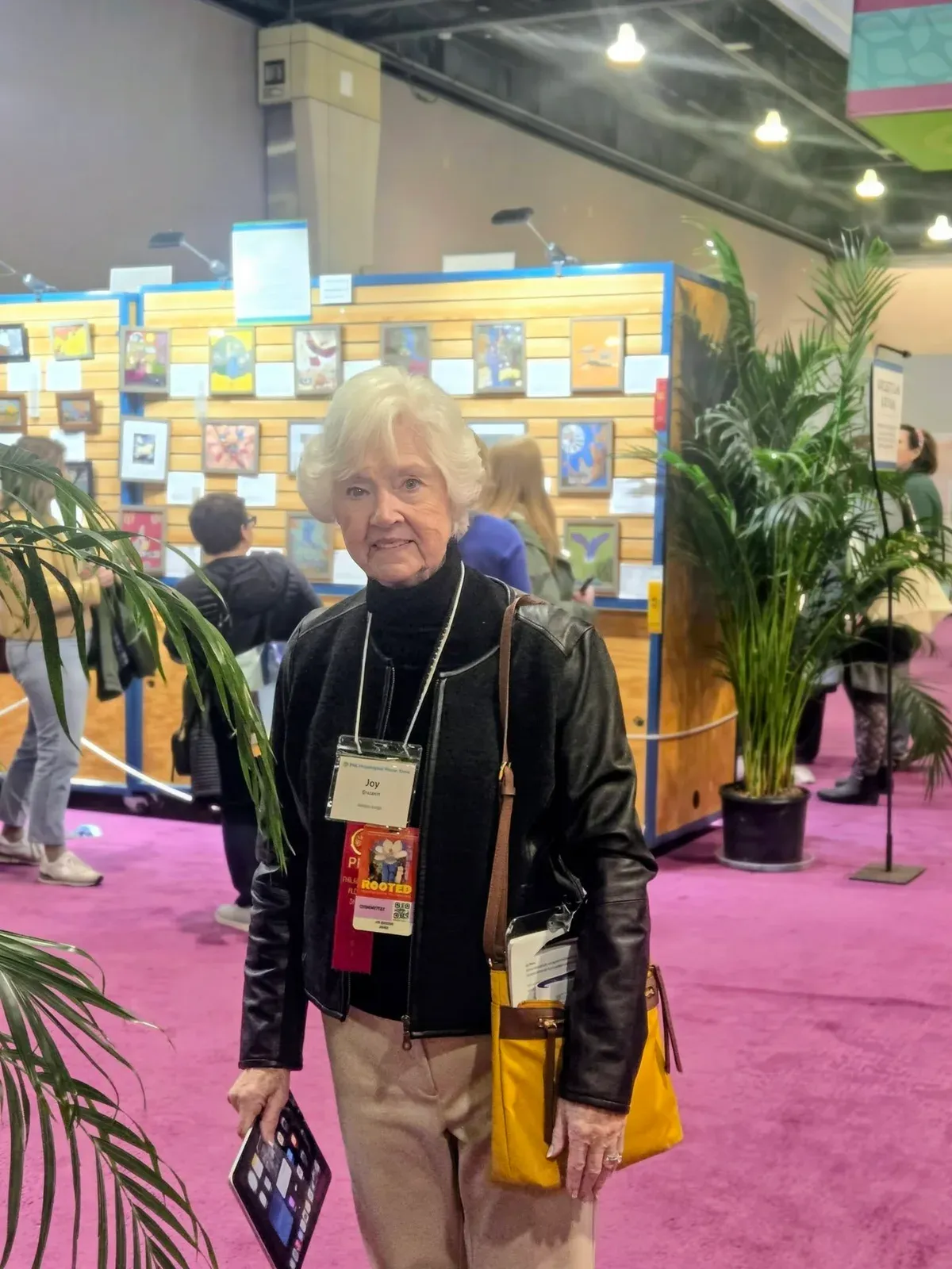 Joy Ericson standing in front of a wall of framed floral entries, wearing her judge's badge at the Philadelphia Flower Show.
